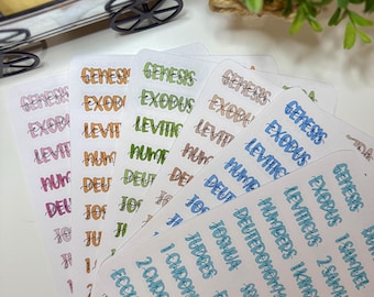 May include: A selection of Bible book stickers in assorted colours, such as orange, green, and blue. Each sticker displays a Bible book title in a handwritten font. The stickers are arranged in a fan shape.
