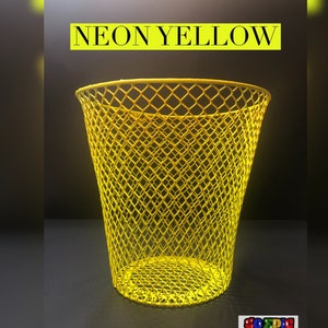 Puede incluir: Un cubo de basura de alambre amarillo ne&oacute;n brillante con un patr&oacute;n de malla en forma de diamante. El cubo est&aacute; vac&iacute;o y se encuentra sobre una superficie oscura. El texto "NEON YELLOW" est&aacute; escrito en letras negras en la parte superior de la imagen.