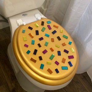 Könnte beinhalten: Goldfarbener Toilettensitz mit einem bunten Mosaik aus rechteckigen Fliesen.