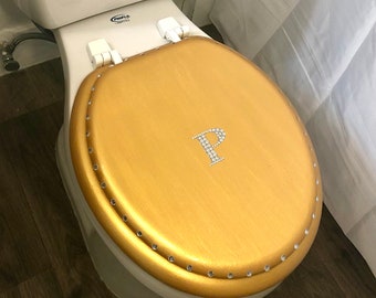 May include: Gold toilet seat cover with a rhinestone 'P' in the center. The cover has a beaded edge.