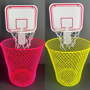 Puede incluir: Dos canastas de baloncesto en miniatura con redes unidas a cubos de basura de malla rosa y amarilla. Las canastas son blancas con ribetes rojos.