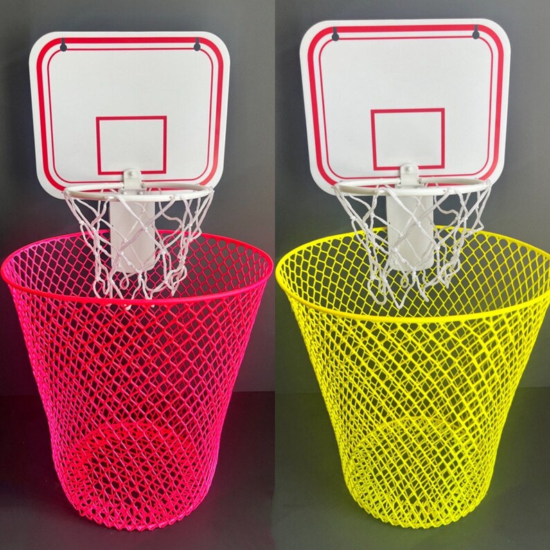Puede incluir: Dos canastas de baloncesto en miniatura con redes unidas a cubos de basura de malla rosa y amarilla. Las canastas son blancas con ribetes rojos.