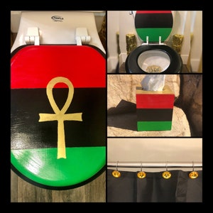 May include: A bathroom decor set featuring a toilet seat, tissue box, and shower curtain. The toilet seat and tissue box are painted with red, black, and green stripes, and a gold ankh symbol. The shower curtain has gold-colored shower curtain rings.