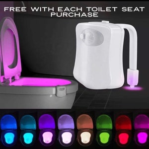 May include: A white LED toilet night light with a motion sensor. The toilet seat is illuminated with a pink glow. The image also shows a variety of colors the light can display, including blue, green, and red. Text on the image reads "FREE WITH EACH TOILET SEAT PURCHASE".