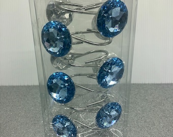 Puede incluir: Un paquete de seis anillos de cortina de ducha de cristal azul. Los anillos son plateados y tienen un respaldo de plástico transparente.