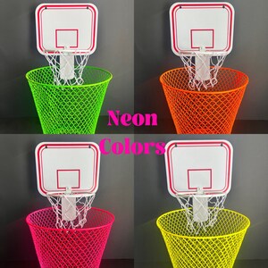 Puede incluir: Cuatro cubos de basura de color ne&oacute;n con un mini aro de baloncesto sujeto a la parte superior. Los cubos de basura son verdes, naranjas, rosas y amarillos.