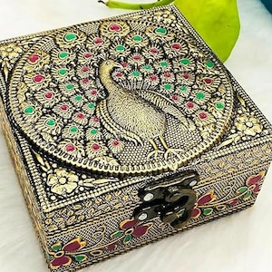 Könnte beinhalten: Verzierte, goldfarbene Box mit einem Pfau-Design auf dem Deckel. Der Pfau ist von roten und grünen Akzenten umgeben. Die Box hat ein dekoratives Blumenmuster und einen Metallverschluss.