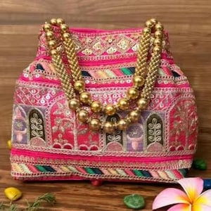 May include: A pink embroidered handbag with a gold beaded handle. The bag features intricate patterns in various colours, including pink, green, and gold. The bag is decorated with gold embellishments and has a rounded shape.