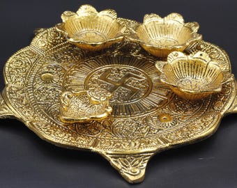May include: Ornate gold-colored metal tray with four flower-shaped bowls. The tray features detailed embossed patterns and a central emblem. The design suggests a cultural or religious significance, possibly for decorative or ceremonial use.