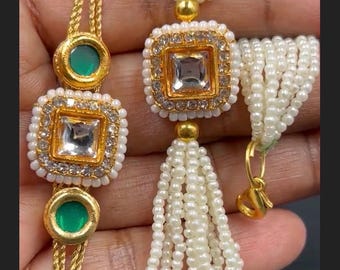 May include: Two bracelets featuring gold-tone metal settings. One bracelet has a central square clear stone surrounded by small white beads and two green circular accents. The other features a square clear stone and multiple strands of white pearls.