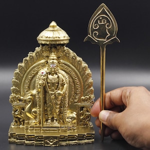 May include: Gold-colored metal statue of a Hindu deity with a staff, sitting on a throne with a decorative arch. The statue is on a base with intricate details. A separate gold-colored metal staff with a decorative top is included.