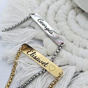 May include: Two personalised bracelets with silver and gold chains. The silver chain bracelet has a silver tag with the name "Georgia" and a heart symbol. The gold chain bracelet has a gold tag with the name "Elisavet" and a heart symbol.
