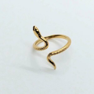 May include: A gold-toned snake ring with a textured finish. The snake is coiled around the ring band, with its head raised and facing forward.