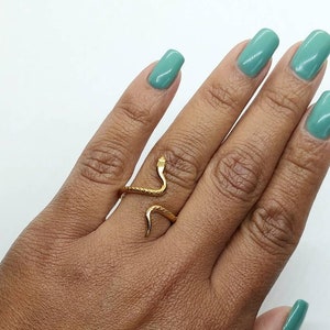 May include: A gold snake ring with a textured body. The ring is worn on the middle finger of a hand with light green nail polish.