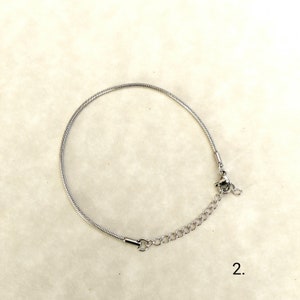 May include: A silver snake chain bracelet with a lobster clasp fastening. The bracelet is on a white background with the number "2." written below it.