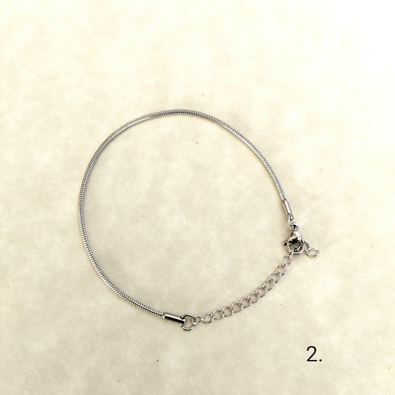 May include: A silver snake chain bracelet with a lobster clasp fastening. The bracelet is on a white background with the number "2." written below it.