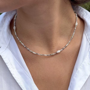Puede incluir: Un collar de cuentas plateadas y blancas con peque&ntilde;as cuentas de imitaci&oacute;n de perlas y cuentas ovaladas m&aacute;s grandes.