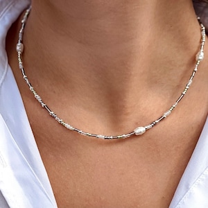 Puede incluir: Un collar de cuentas plateadas y blancas con detalles de perlas. El collar es delicado y presenta peque&ntilde;as cuentas redondas.