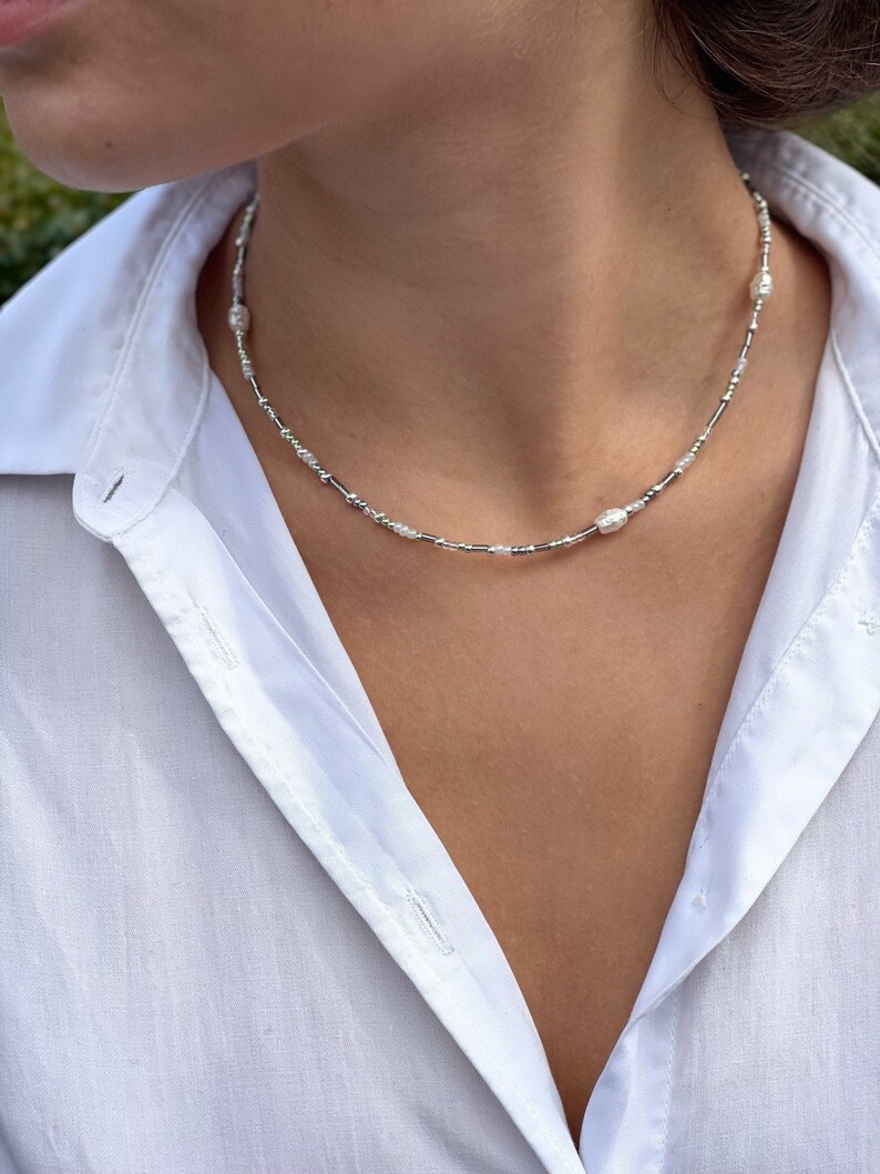 Puede incluir: Un collar de cuentas plateadas y blancas con peque&ntilde;as cuentas de imitaci&oacute;n de perlas y cuentas ovaladas m&aacute;s grandes.