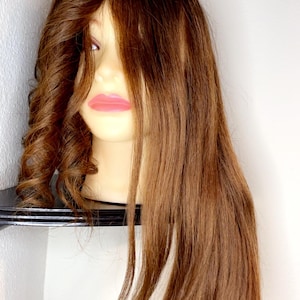 Puede incluir: Una cabeza de maniquí marrón con cabello largo y liso de color marrón. El cabello está peinado con algunos rizos sueltos en la parte superior.