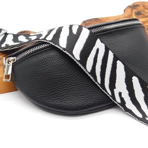 May include: Black leather bum bag with a zebra print strap. The bag features a silver zip and hardware. The strap has a striking black and white zebra stripe pattern. The bag is curved in shape.