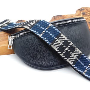 May include: Black leather bum bag with a silver zip and a blue, black, and white tartan strap. The strap is adjustable and has silver hardware. The bag is on a wooden surface.