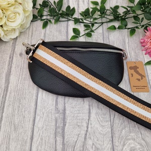 May include: Black leather bum bag with a silver zip and a wide strap with black, gold, and white stripes. The bag has a textured finish and a tag reading "Genuine Leather Made in Italy."