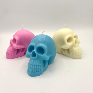 May include: Three skull-shaped candles in pink, blue, and white. The candles are made of wax and have a detailed skull design.
