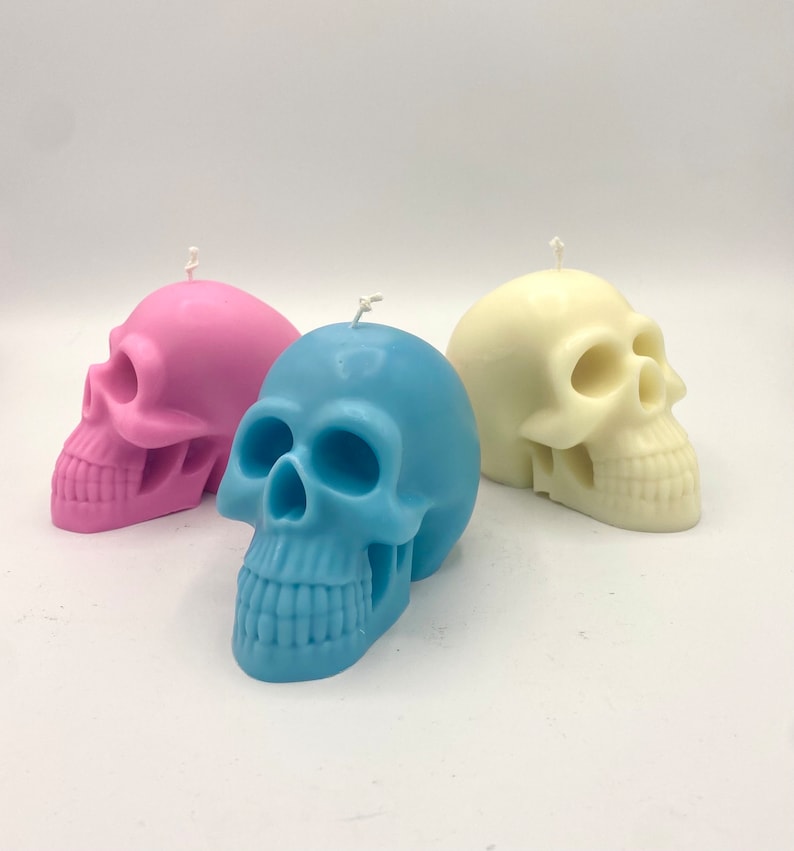 May include: Three skull-shaped candles in pink, blue, and white. The candles are made of wax and have a detailed skull design.