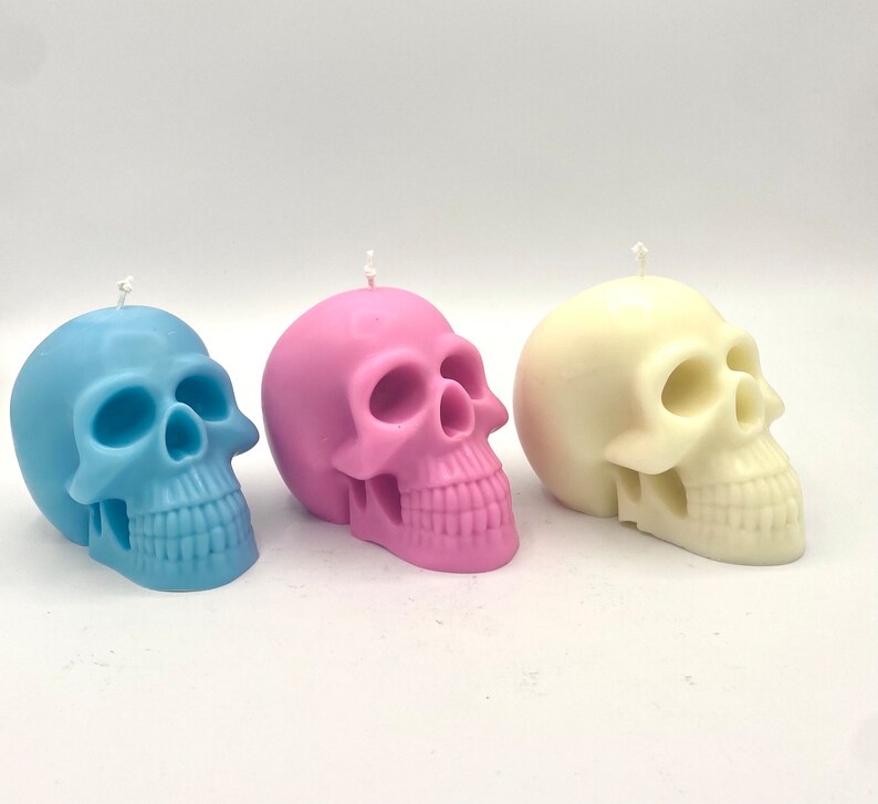 May include: Three skull-shaped candles in different colors: light blue, pink, and white. The candles are made of wax and have a realistic skull design.