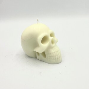 May include: A white skull-shaped candle with a detailed face and a small wick on top.