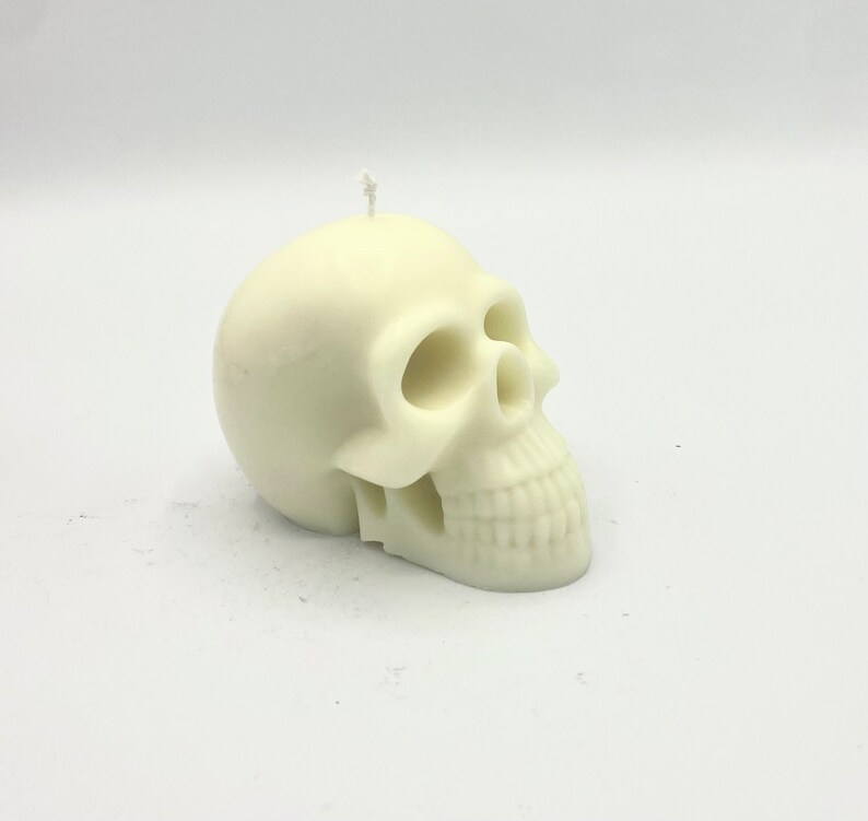 May include: A white skull-shaped candle with a detailed face and a small wick on top.