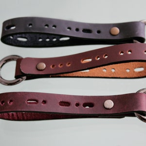 Peut inclure: Trois porte-clés en cuir avec des anneaux métalliques. Les porte-clés sont en noir, marron et bordeaux.