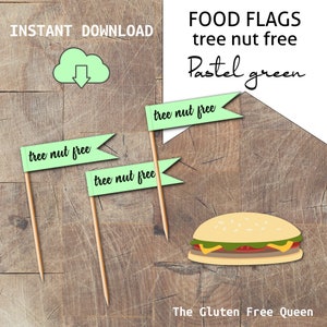 Puede incluir: Cuatro banderas de comida verde pastel con el texto "tree nut free" impreso en ellas. Las banderas están en pinchos de madera y están dispuestas sobre una superficie de madera. Una hamburguesa con un pan verde se encuentra en la esquina inferior derecha de la imagen. El texto "FOOD FLAGS tree nut free Pastel green" se encuentra en la esquina superior derecha de la imagen.