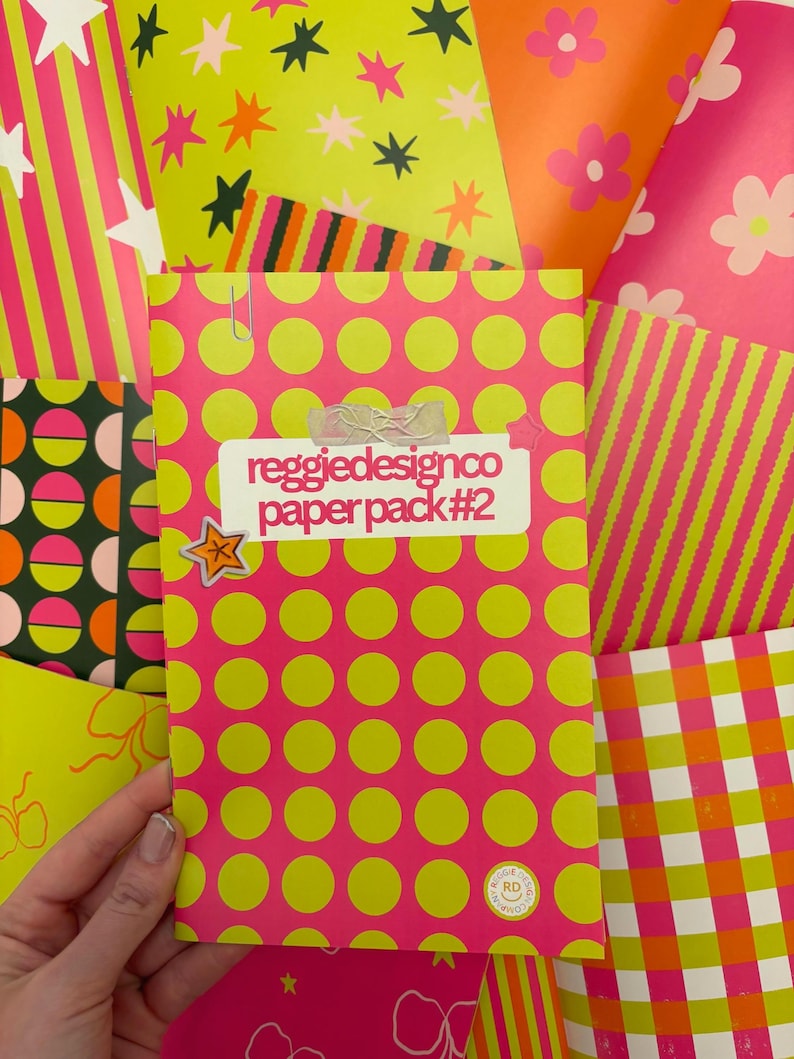 May include: A collection of colorful patterned papers. The central paper pack, labeled "reggiedesignco paper pack #2", features a pink background with large yellow polka dots. Other papers display stripes, stars, and floral designs in vibrant pink, orange, and green.