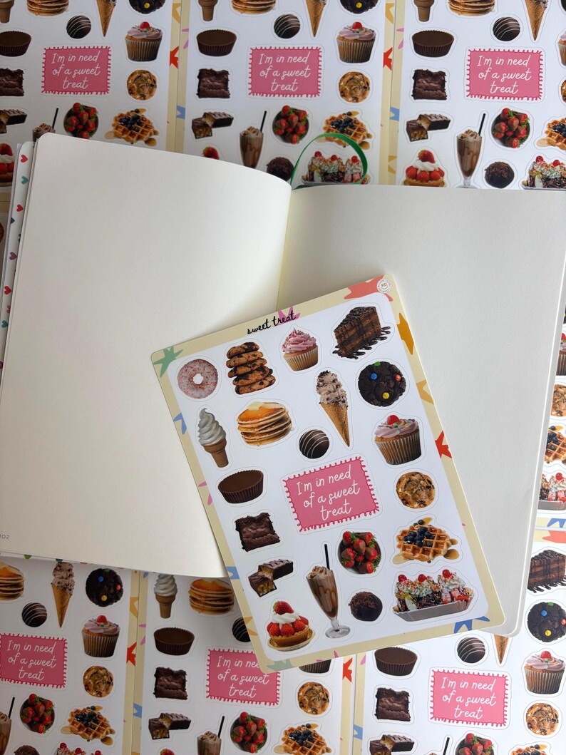 May include: An open notebook with blank pages and a sticker sheet displaying an assortment of desserts, including donuts, cupcakes, and ice cream. The sticker sheet has the text "sweet treat" and "I'm in need of a sweet treat."
