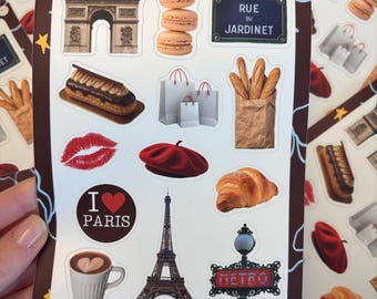 May include: A sticker sheet with a Parisian theme. The stickers feature the Eiffel Tower, Arc de Triomphe, French pastries, shopping bags, and the text "I Love Paris". The text "j'aime paris" is also visible.