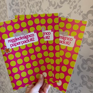 May include: Three paper packs with a bright pink polka dot pattern and lime green dots. Each pack has a white label with the text "reggiedesignco paper pack #2". A small star sticker is visible on one pack.
