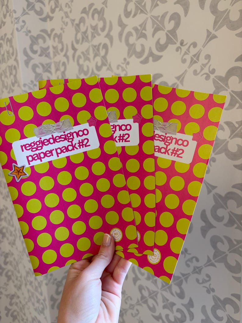 May include: Three paper packs with a bright pink polka dot pattern and lime green dots. Each pack has a white label with the text "reggiedesignco paper pack #2". A small star sticker is visible on one pack.