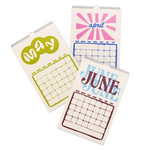 May include: Three wall calendars with spiral binding at the top. The May page features lime green text and a grid. The April page displays pink sunburst graphics with blue text and a grid. The June page shows blue and dark red text with a grid.