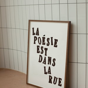 Puede incluir: Una impresi&oacute;n enmarcada con el texto "LA PO&Eacute;SIE EST DANS LA RUE" en letras negras sobre un fondo blanco.
