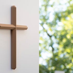 Peut inclure: Une croix en bois brun montée sur un mur blanc. La croix est nette, tandis que l'arrière-plan est flou et montre un arbre vert feuillu.