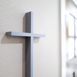 Peut inclure: Une croix en bois gris mont&eacute;e sur un mur blanc. La croix est simple et de design moderne.