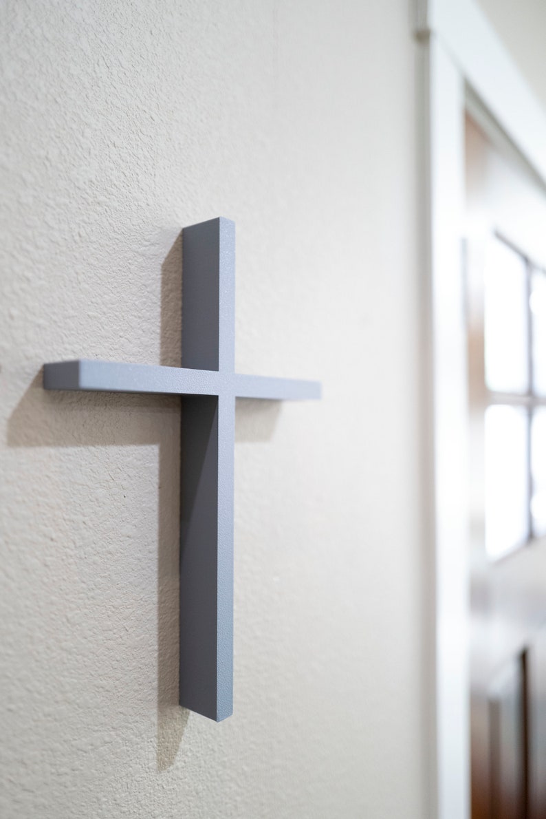 Peut inclure: Une croix en bois gris mont&eacute;e sur un mur blanc. La croix est simple et de design moderne.