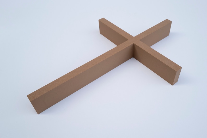 Peut inclure: Une simple croix en bois de couleur brun clair. La croix est pos&eacute;e &agrave; plat sur une surface blanche.