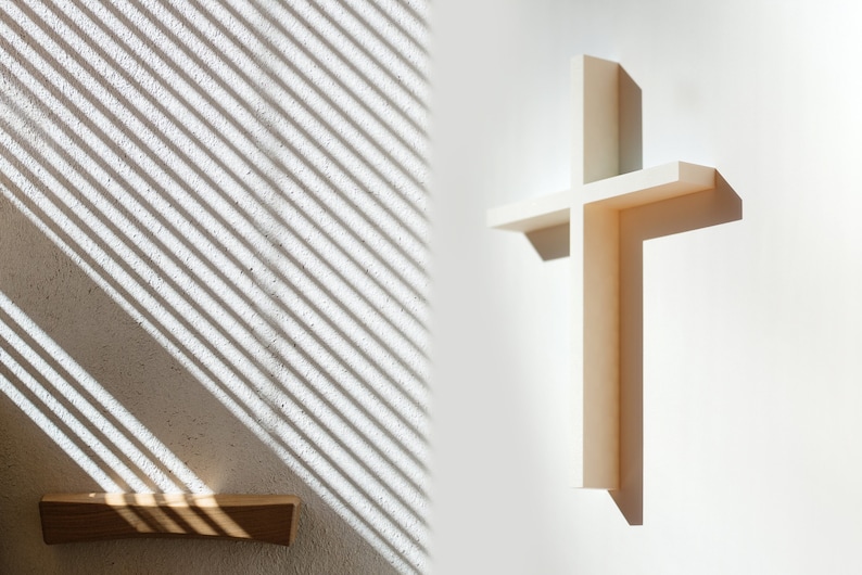 Peut inclure: Une croix en bois blanc mont&eacute;e sur un mur blanc avec une ombre projet&eacute;e par la croix. Le mur pr&eacute;sente un motif de lumi&egrave;re et d'ombre provenant d'un store.