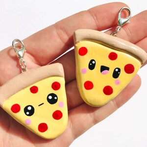 May include: Two cute pizza slice charms with happy faces and red pepperoni. The charms are made of polymer clay and have a silver chain attached.