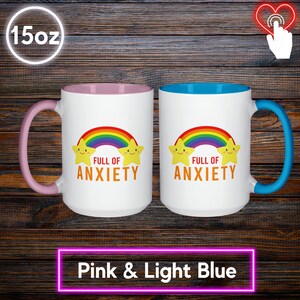 May include: Two white 15oz mugs with colorful designs. One mug has a pink interior and handle, the other has a light blue interior and handle. Both mugs feature a rainbow, smiling stars, and the text "FULL OF ANXIETY".