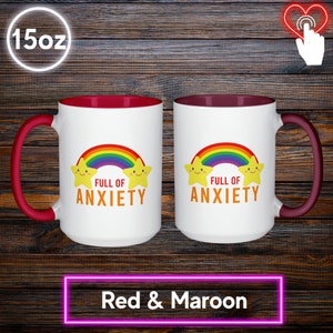 May include: Two white 15oz mugs with red handles and maroon interiors. Each mug features a rainbow, two smiling stars, and the text "FULL OF ANXIETY" in orange. The mugs are labeled "Red & Maroon" at the bottom.