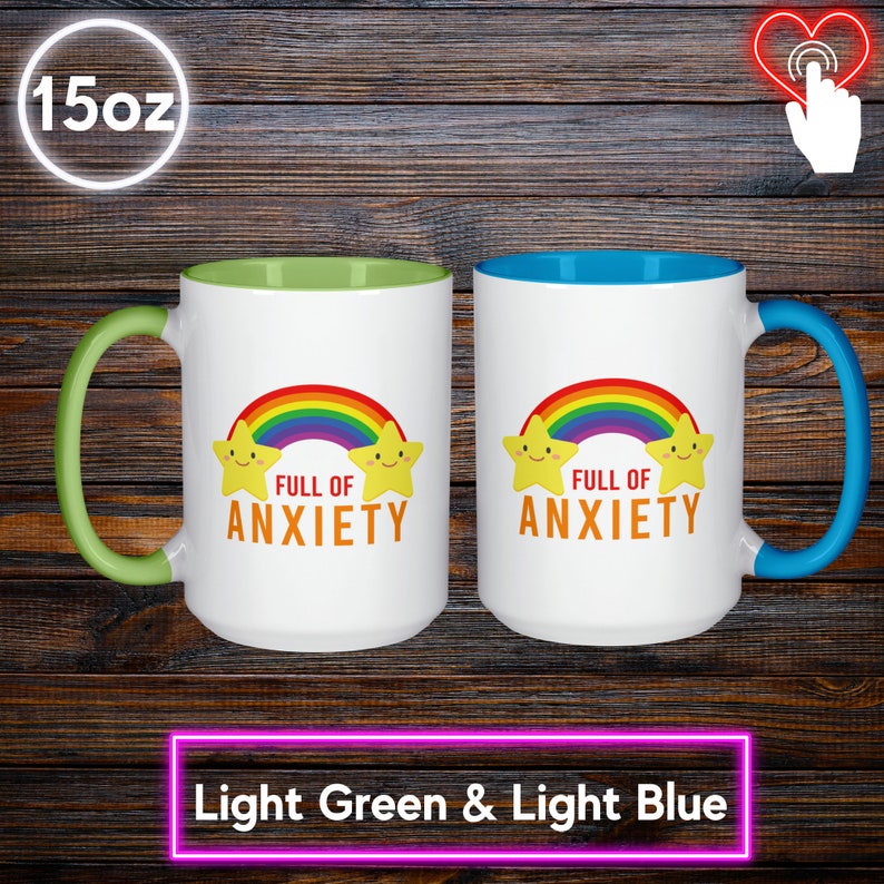 May include: Two white 15oz mugs with a light green and light blue interior and handle. Each mug features a rainbow and smiling star design with the text "FULL OF ANXIETY" in orange. The mugs are on a dark wood background.